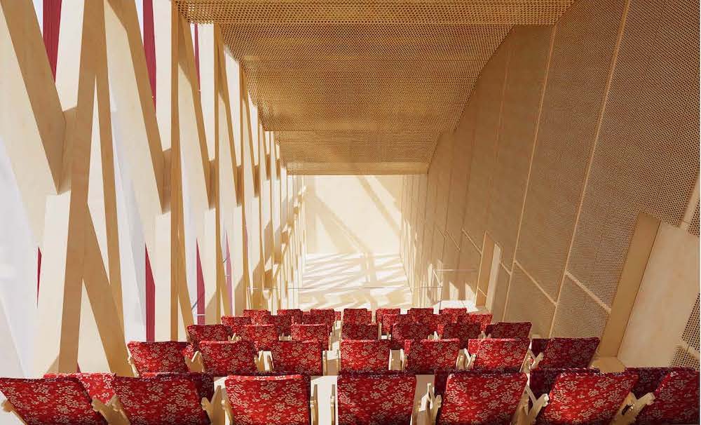 Rows of red theater seats with a view of a stage beyond, with timber wall framing exposed on one side letting light into the space.