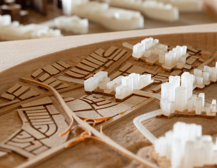 Large site model with people huddled in background looking together at an an architectural site plan