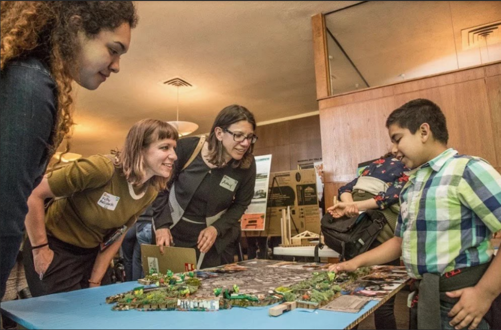 Three people lean over a home project while a child points to it.