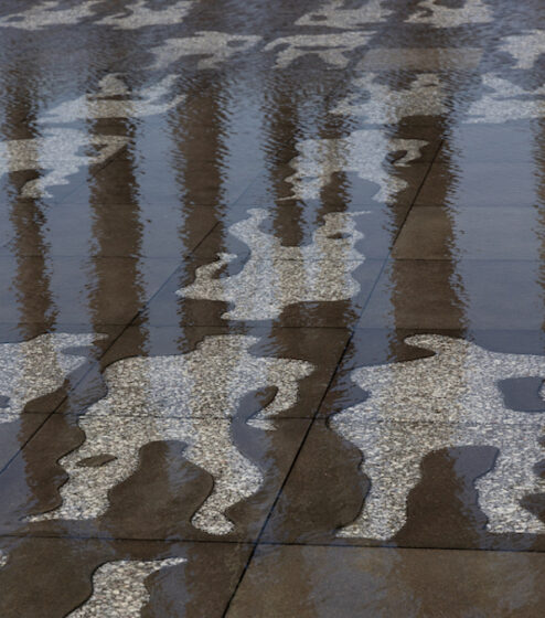 A paved area slick with water, with abstracted human silhouettes incised in a lighter color.