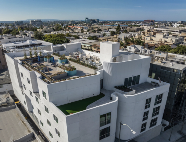 Aerial view of a white apartment building with a rooftop garden with a cityscape in the background