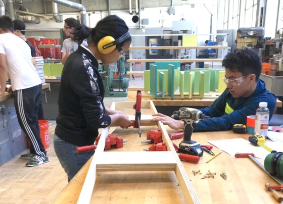 Two young students work on a wooden structure