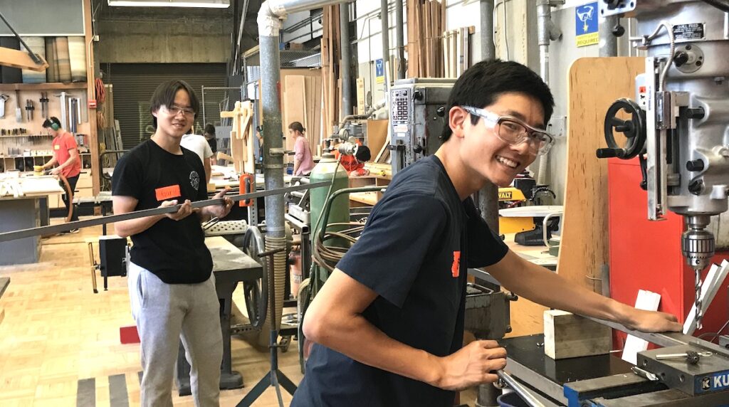 Two smiling teenagers working in wood shop