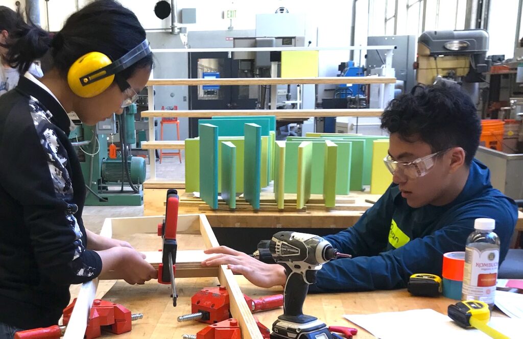 Two teens using a vise to glue wood pieces together