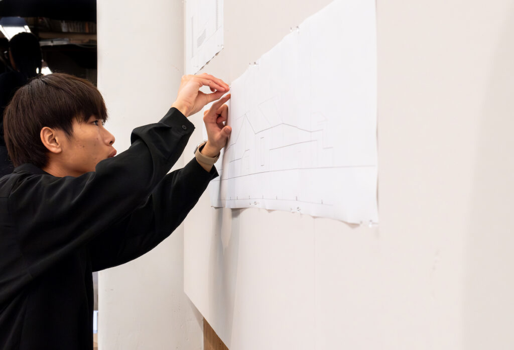 student in black sweater pinning paper to wall