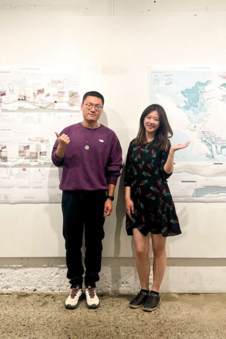 Two students standing in front of drawings pinned to wall