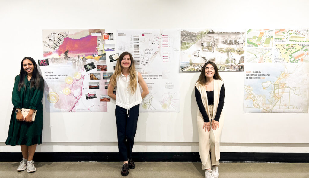 Three students standing in front of drawings pinned to wall