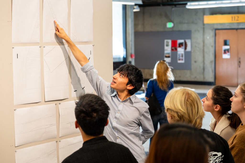 Student pointing to drawing pinned up on wall with other students looking on