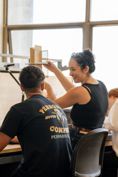 Instructor giving student a desk crit, holding up architectural model