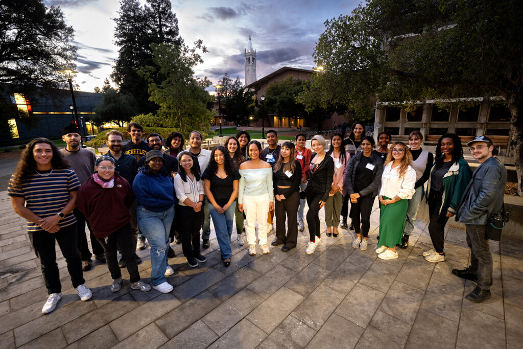 Group of students standing on with Berkeley's bell tower in background.