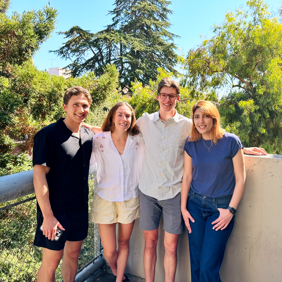 Hack A Haus winners - four students, Ole Seidler, Reily Gibson, Otis Klinbeil, and Sepideh Farnia, smiling on a balcony surrounded by trees.