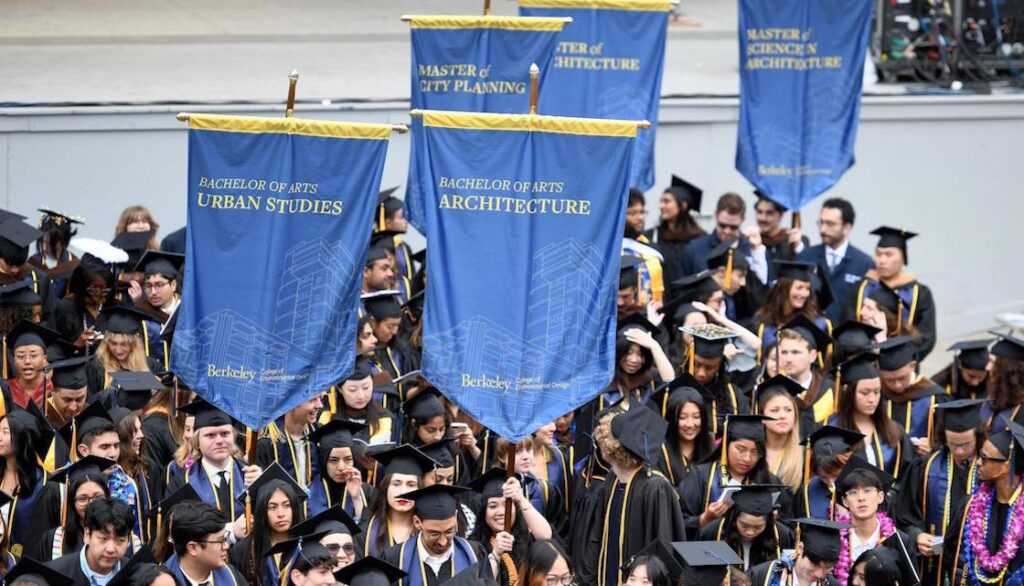 Crowd of graduates in caps and gowns holding various banners with names of degree programs