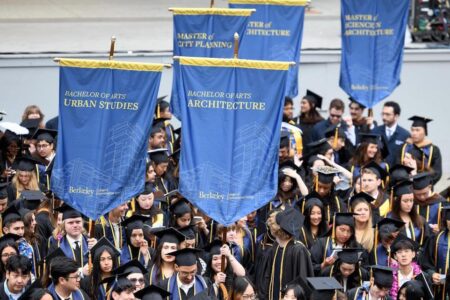 Crowd of graduates in caps and gowns holding various banners with names of degree programs