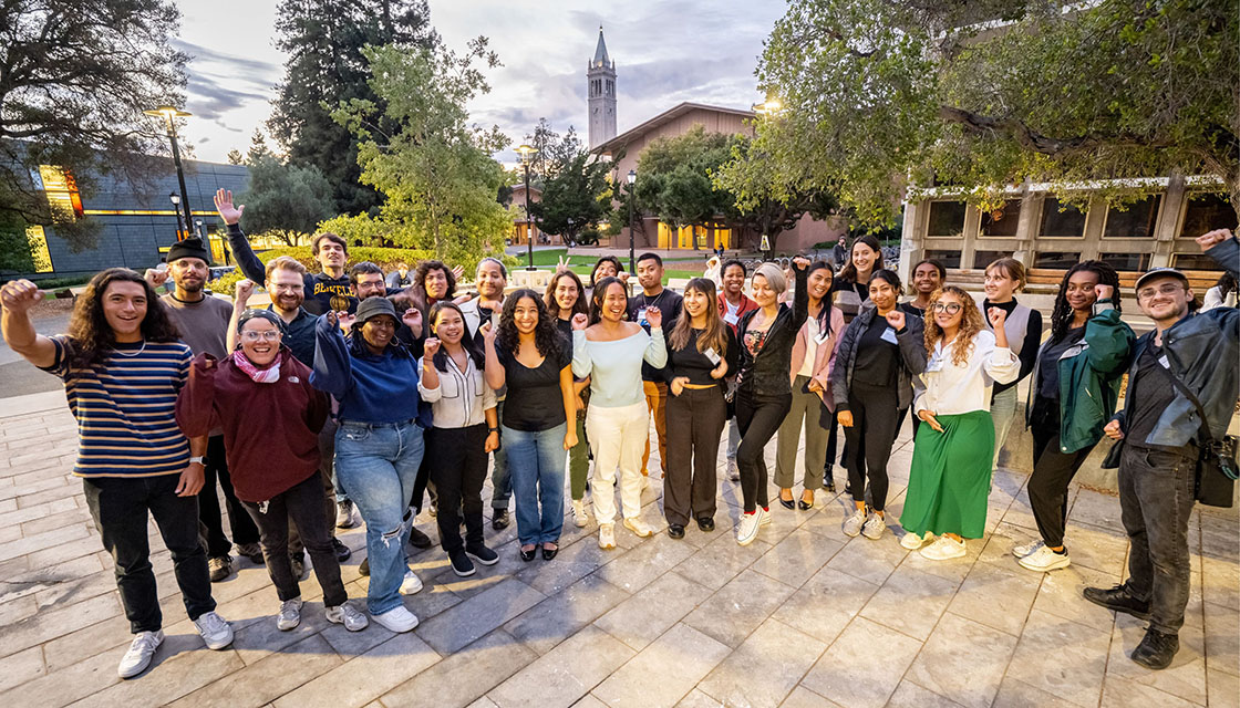 Group of students standing on with Berkeley's bell tower in background.