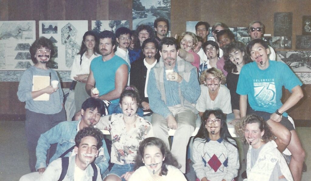 Group of students with fake mustaches to match professor, in middle, posing for camera