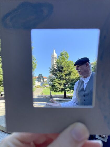 View of landscape architecture professor Chip Sullivan wearing beret with campanile in background, seen through frame held by a thumb