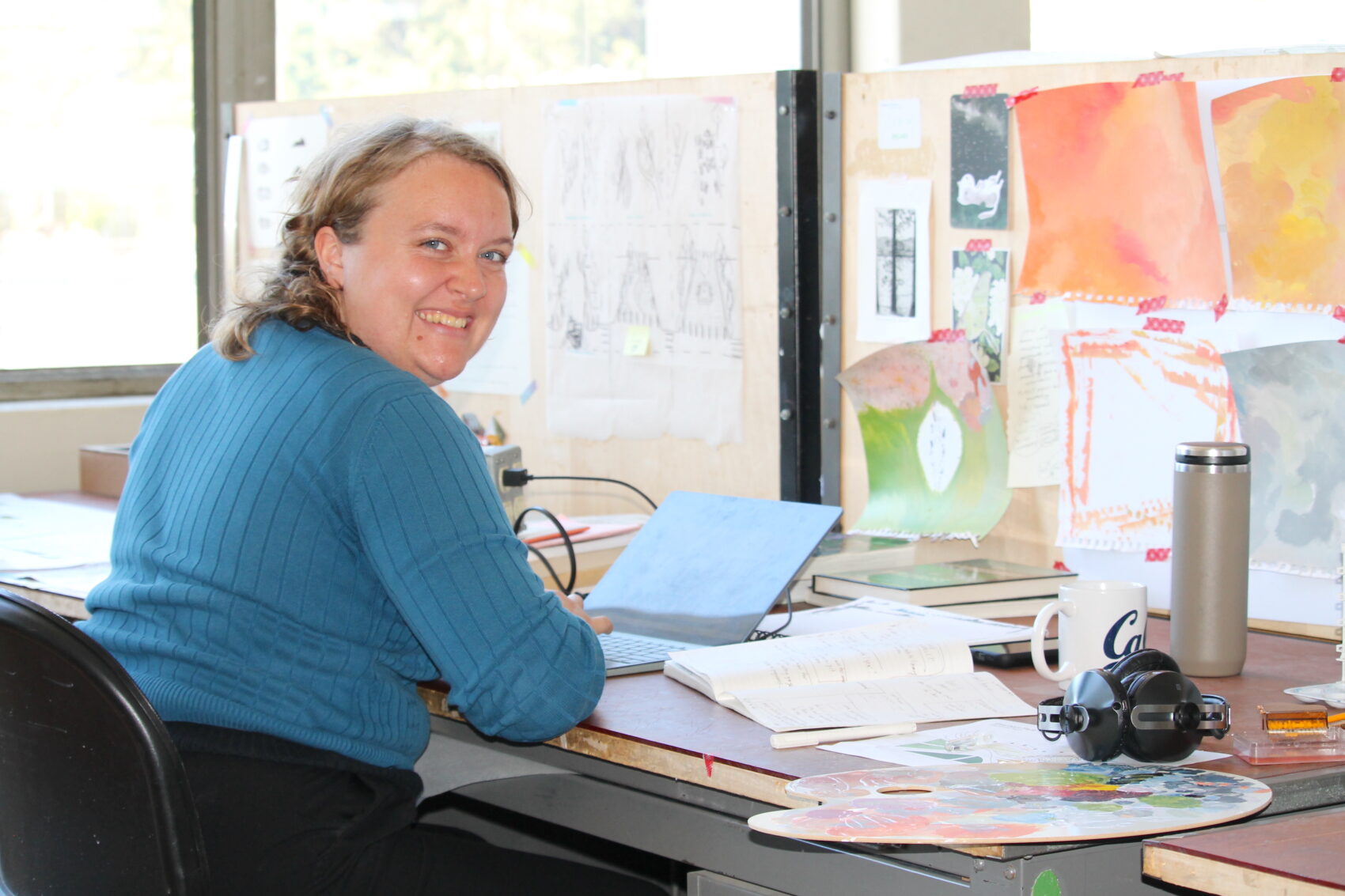 Student sitting in blue sweater, smiling at camera, working in studio