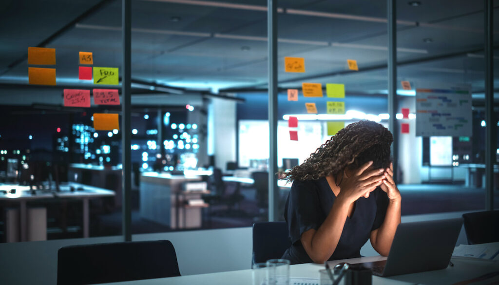 African American woman in front of laptop in office building, holding head in hands