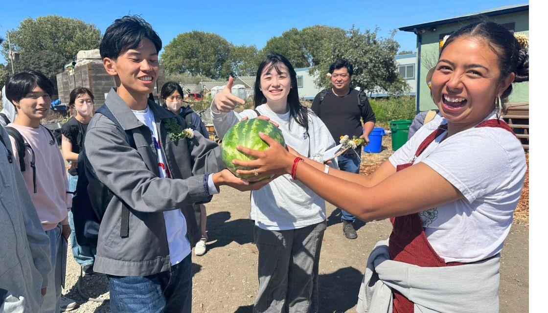 Smiling woman handing a watermelon to a student from Japan