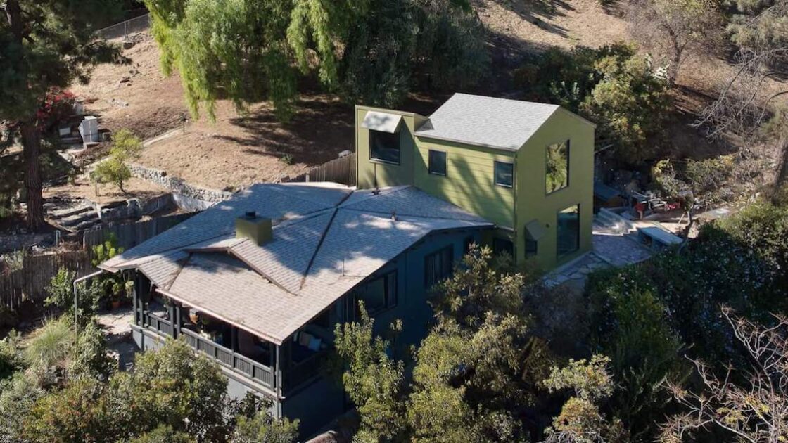 Aerial view of low-lying house with two-story green wood-clad addition