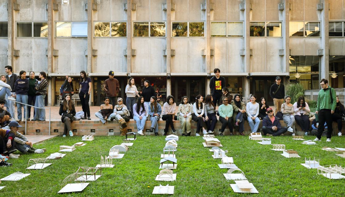Architectural models displayed on lawn with students and building in background