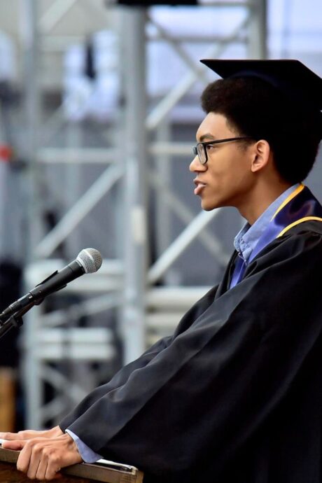 Person in graduation cap and gown speaking into a microphone