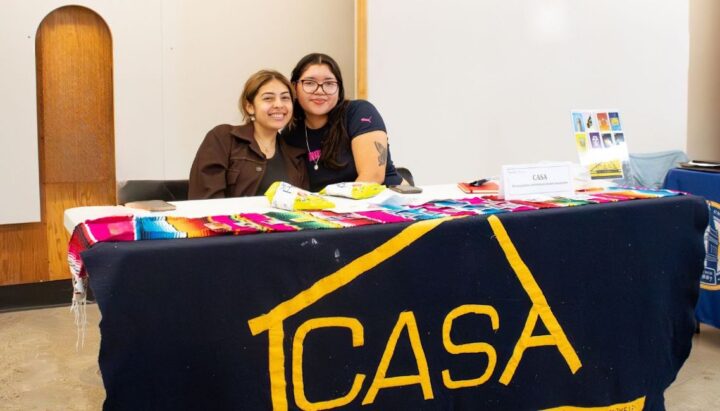 Two students posing at a table with a sign reading CASA