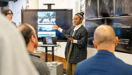Student pointing at monitor while presenting project in front of critics